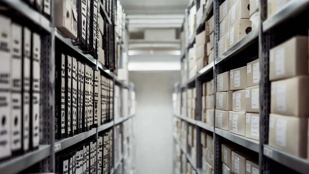 Pasillo de un archivo con estanterías metálicas llenas de cajas y biblioratos