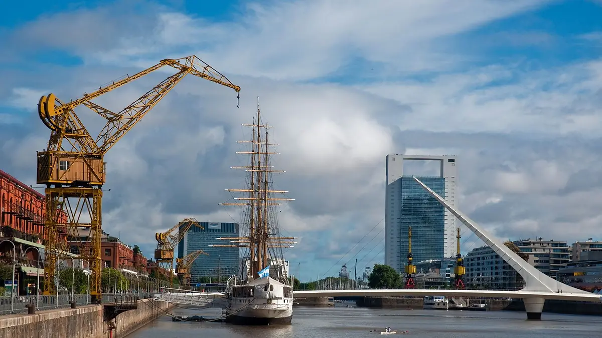 Dique 3 de Puerto Madero con una grúa portuaria antigua, la Fragata Sarmiento y el Puente de la Mujer