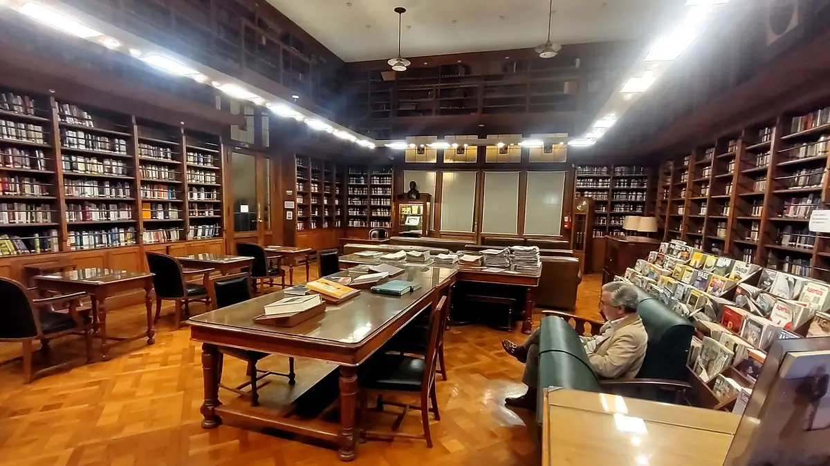 Sala de lectura de la biblioteca del Club Universitario de Buenos Aires, con estanterías de madera y mesas largas