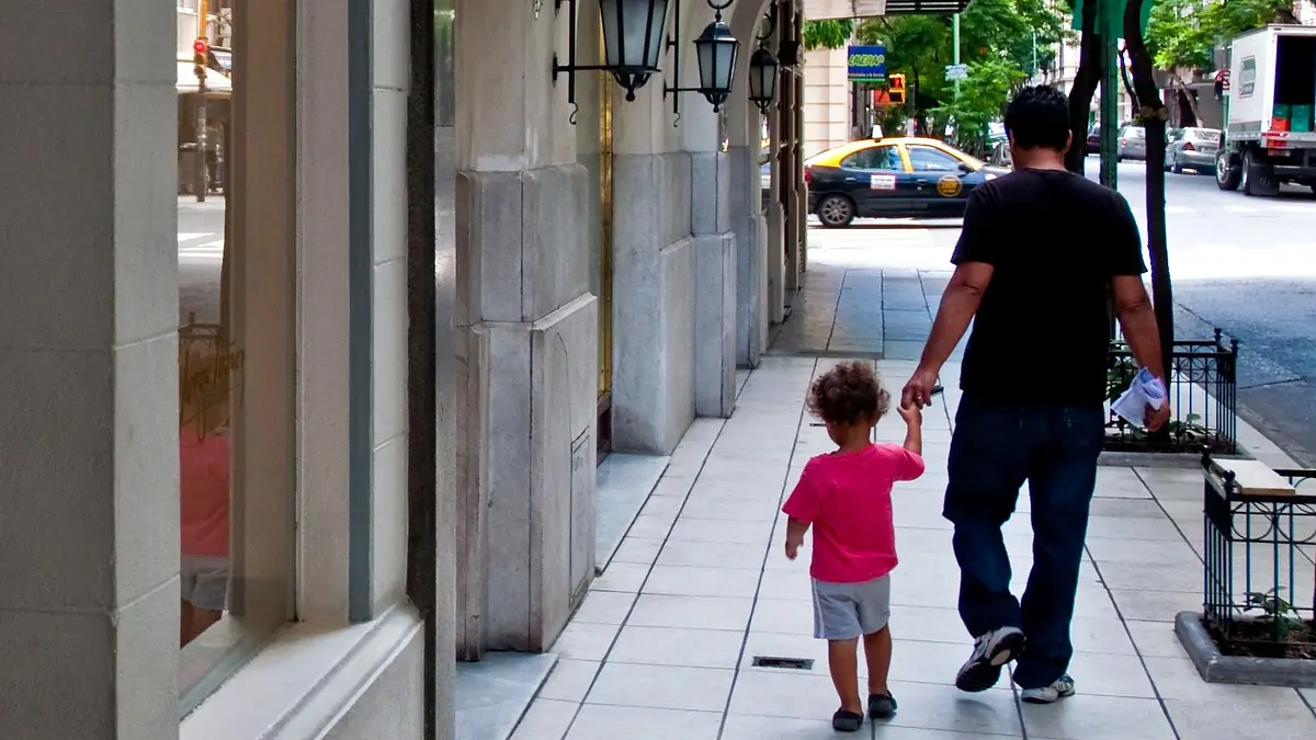 Un padre camina de la mano de su hija pequeña por una vereda arbolada de Recoleta, en Buenos Aires