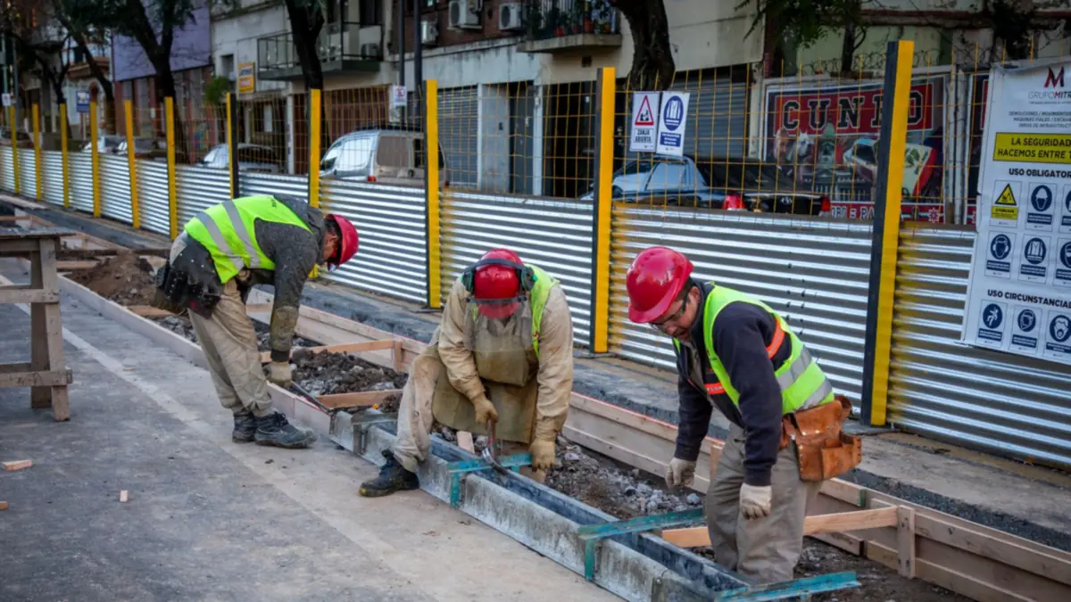 Tres obreros con casco y chaleco reflectivo trabajan en la renovación de la avenida Caseros, en Buenos Aires